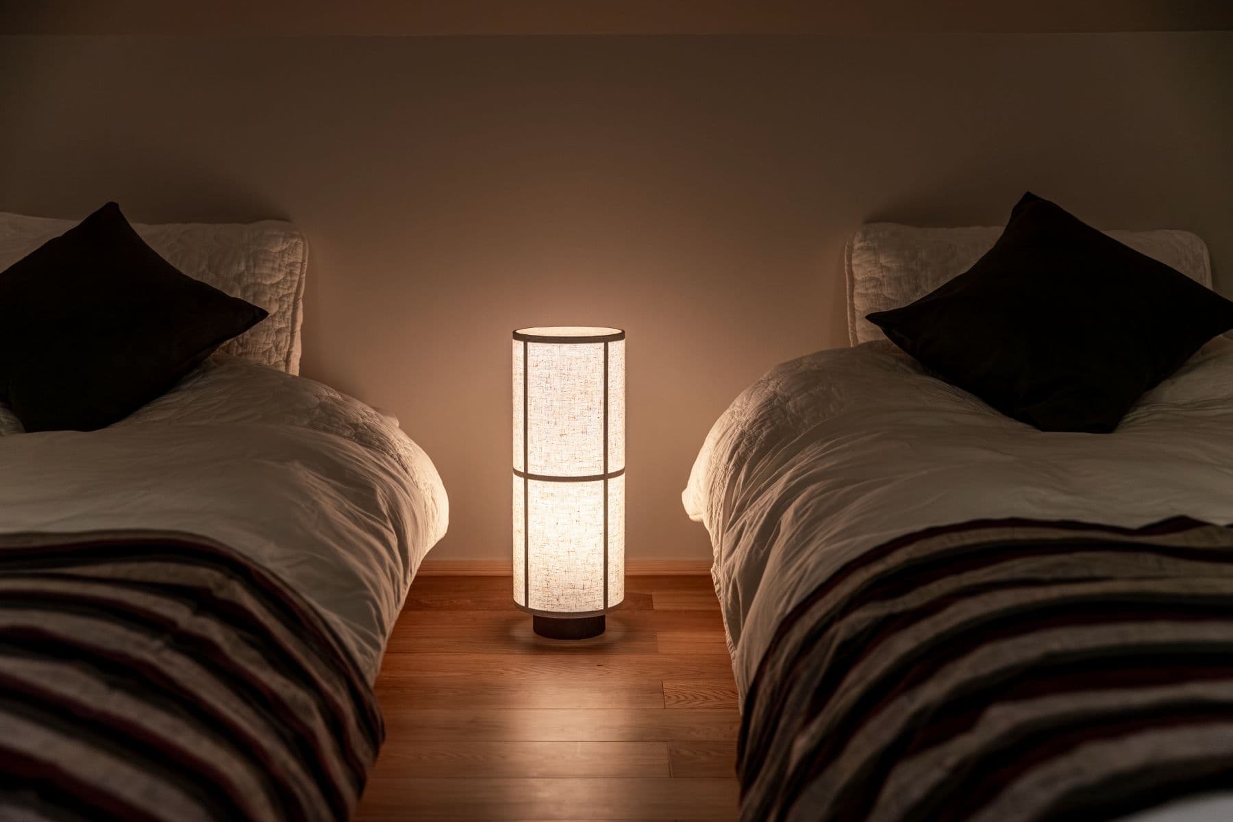 A twin-bed room with a floor lamp glowing between the beds.