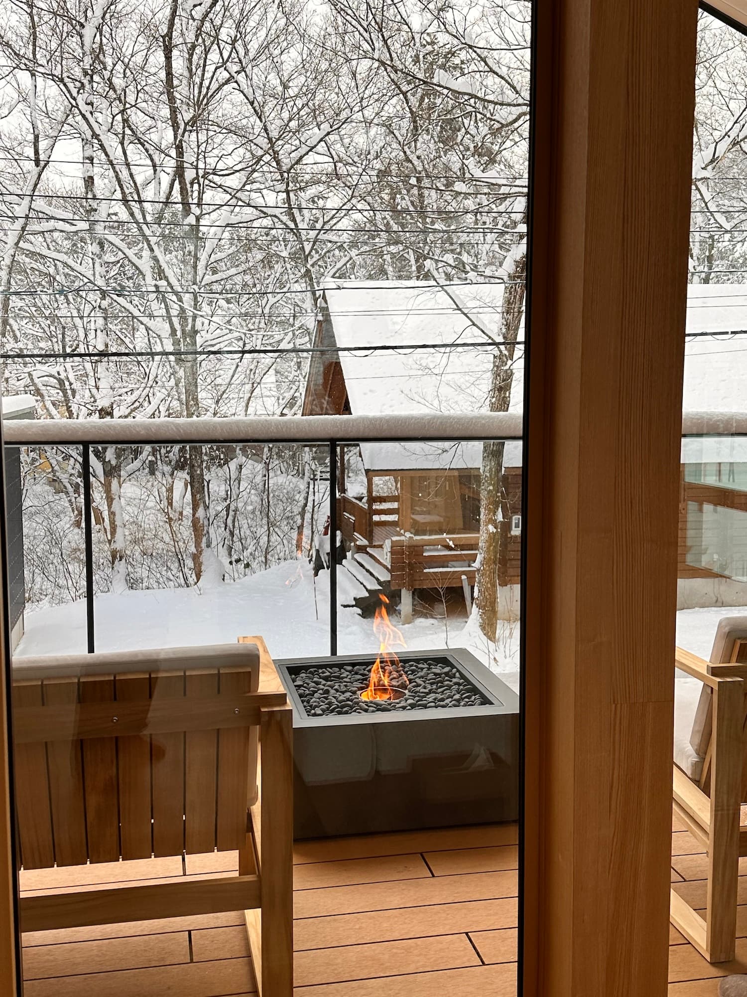 窓越しに望む雪景色のテラス。雪に包まれた森と暖炉の炎が冬の情景を演出する。
